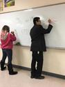 Two students at the whiteboard showing their work for a problem. 