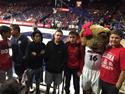 Students smiling for a photo with the sports mascot at a game. 