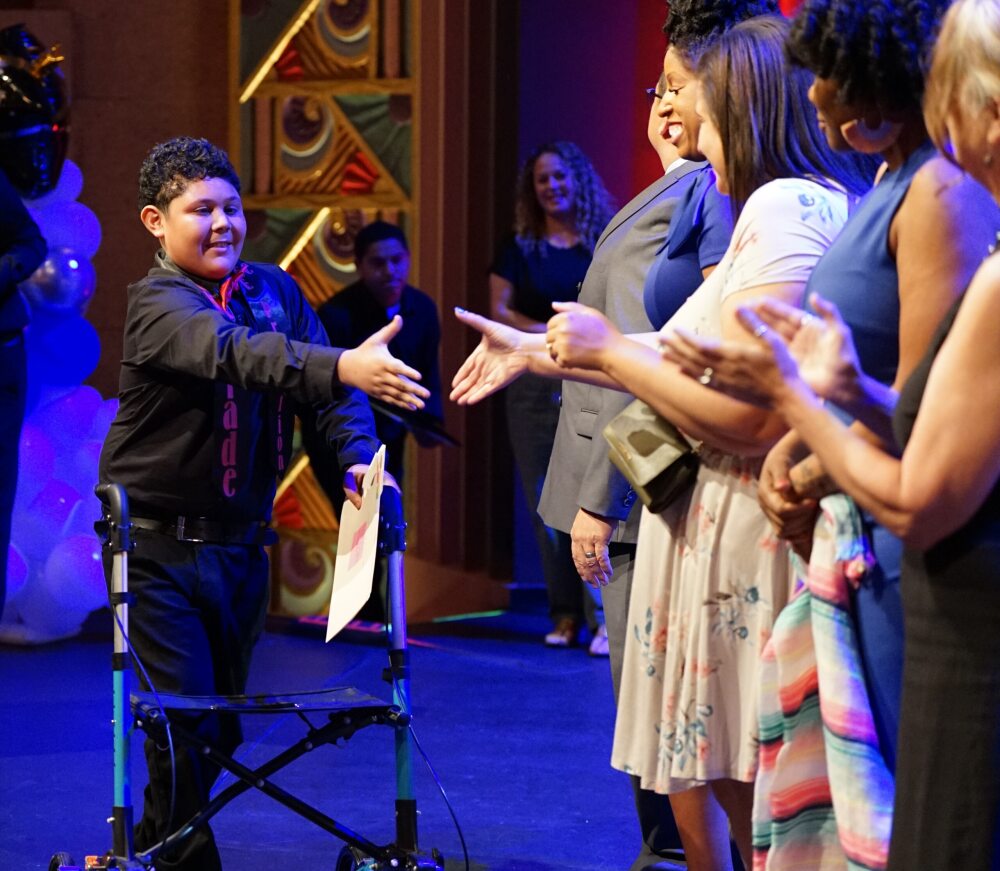 A student reaches out his hand to shake as he receives his 8th grade diploma