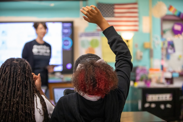 A girl with red curly hair raises her hand
