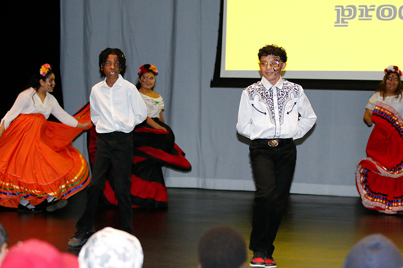 Students in folklorico outfits dance on stage