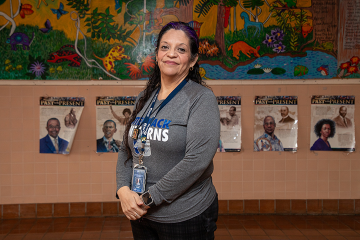 A woman in a gray Utterback shirt smiles in front of a colorful mural