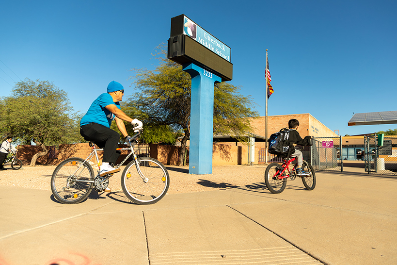 A dad and son bike on the sidewalk in front of the school